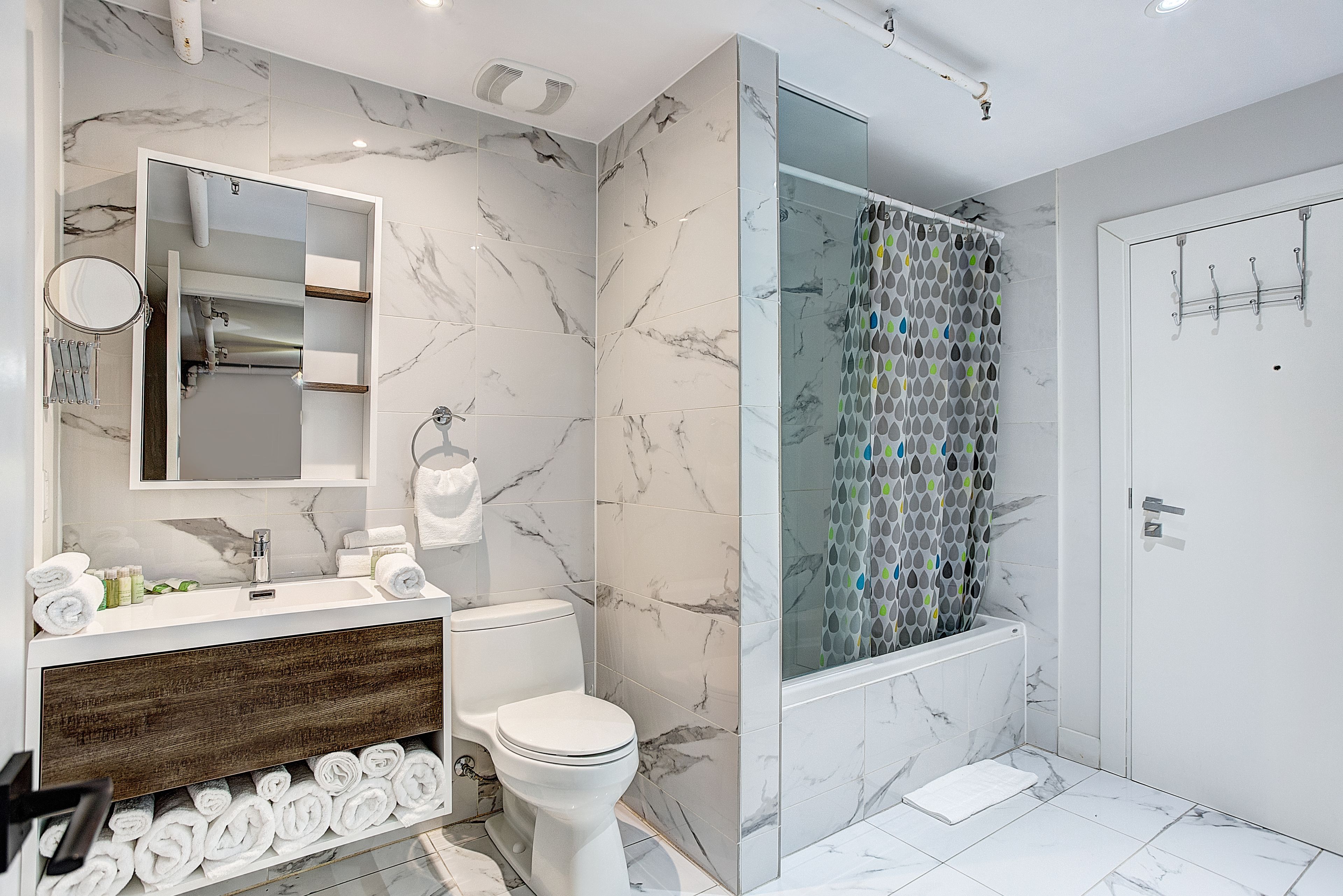 Ein modernes Badezimmer mit Marmorfliesenspiegel, einer Glasdusche und einem Holzbadezimmer-Möbel.