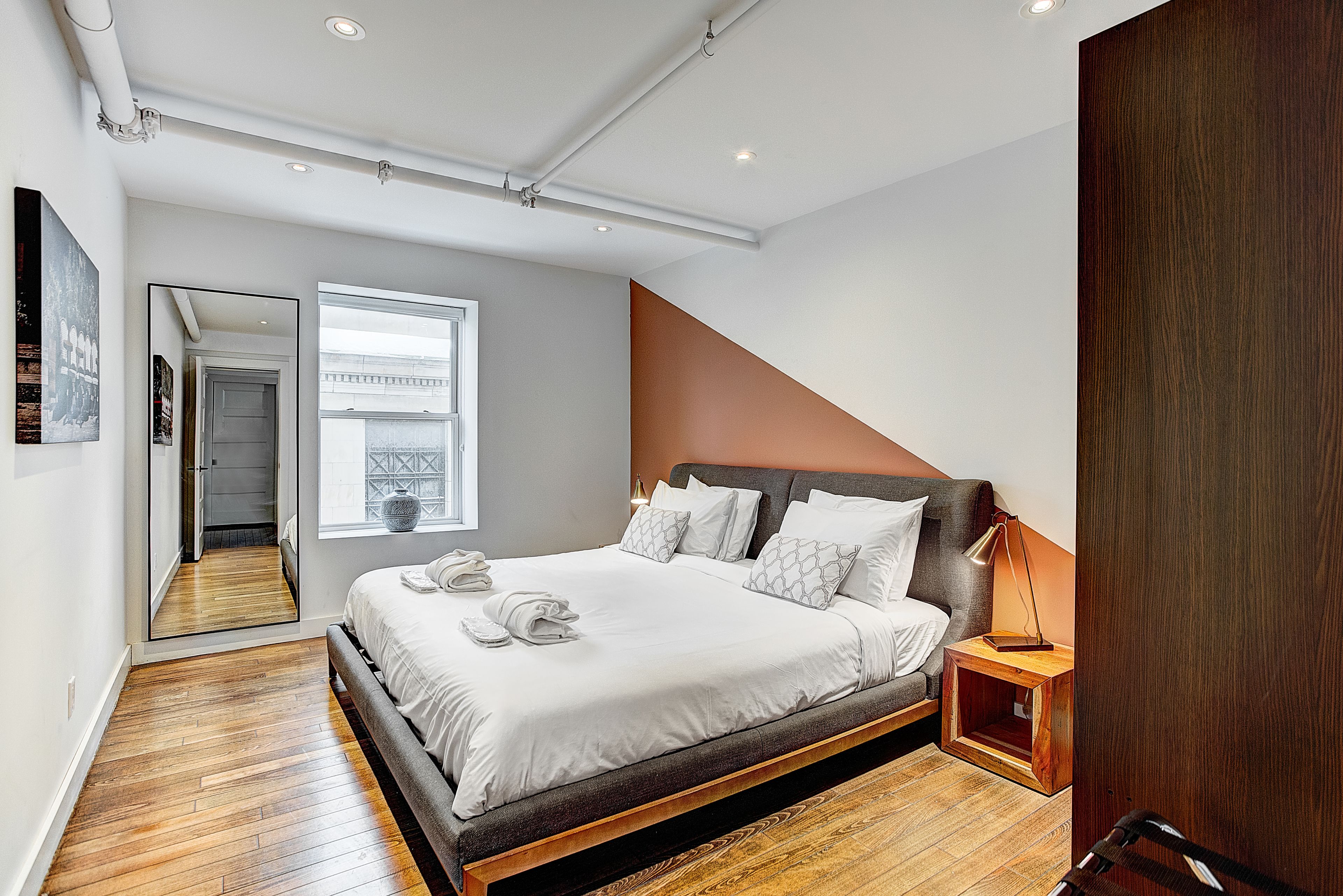 Un dormitorio moderno con una cama grande, una mesita de noche de madera, un espejo y vistas al exterior.