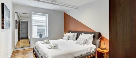 Un dormitorio moderno con una cama grande, una mesita de noche de madera, un espejo y vistas al exterior.