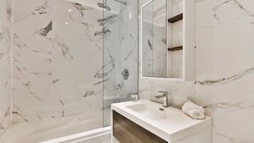 A modern bathroom with a marble shower, a white sink, and a wooden vanity.