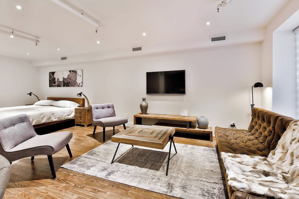 Una habitación de hotel moderna con una cama, dos sillones, un sofá, una mesa de centro y un televisor.