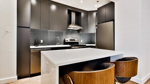 A modern kitchen with dark cabinetry, a white countertop, and stainless steel appliances. - The SFX Old Port (Montreal)