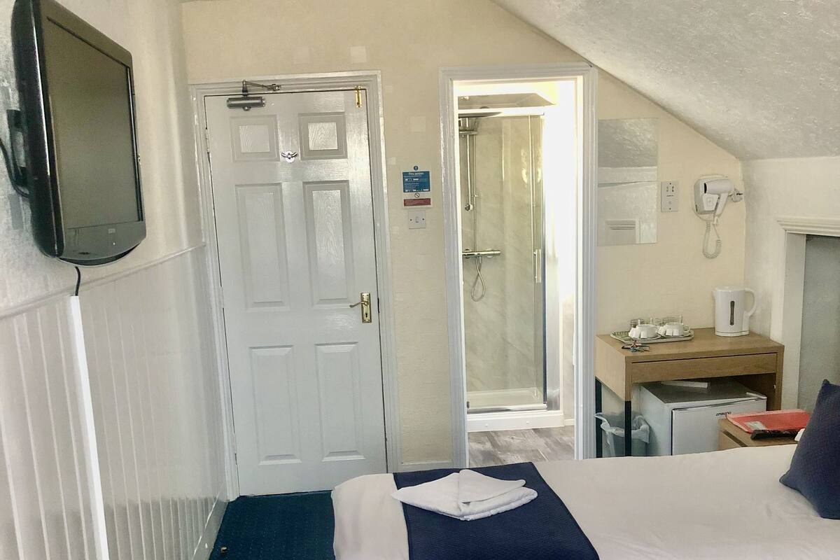 A hotel room with two beds, a TV, a desk with a phone, and a shower area.