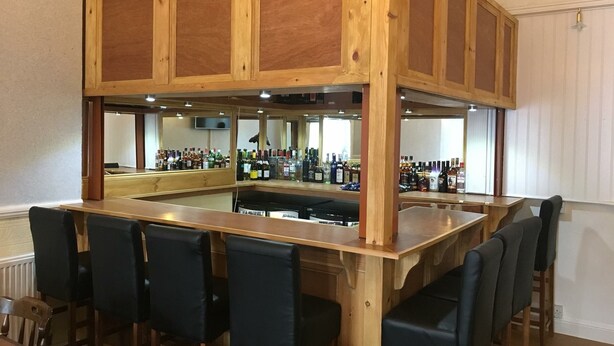 Una zona de bar con paneles de madera, una barra y taburetes.