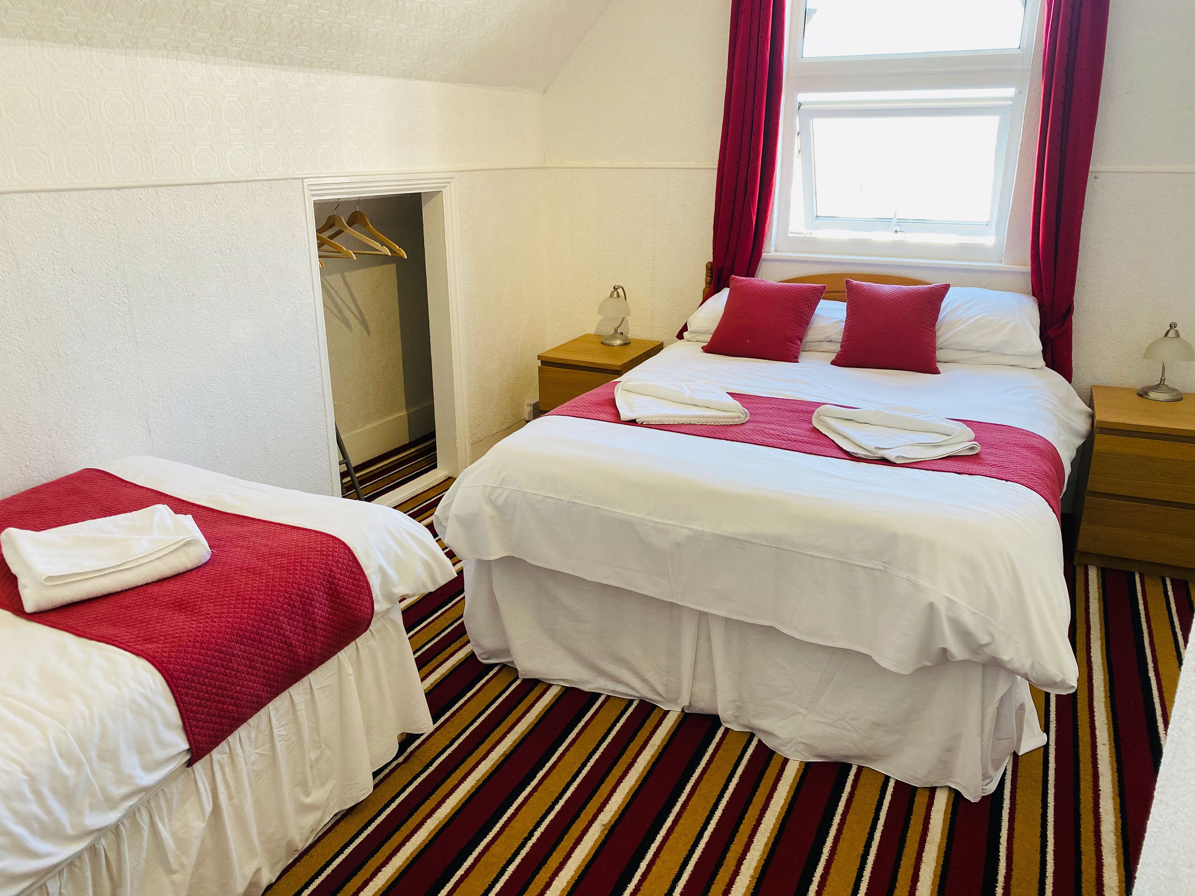 A hotel room with a bed, a smaller bed, a wardrobe, a nightstand, and a window with curtains.