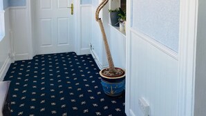 Un pasillo con techo de madera, una puerta blanca, alfombra azul estampada y una planta en maceta.