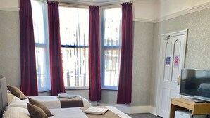 Habitación de hotel con dos camas, cortinas rojas, televisión y escritorio.