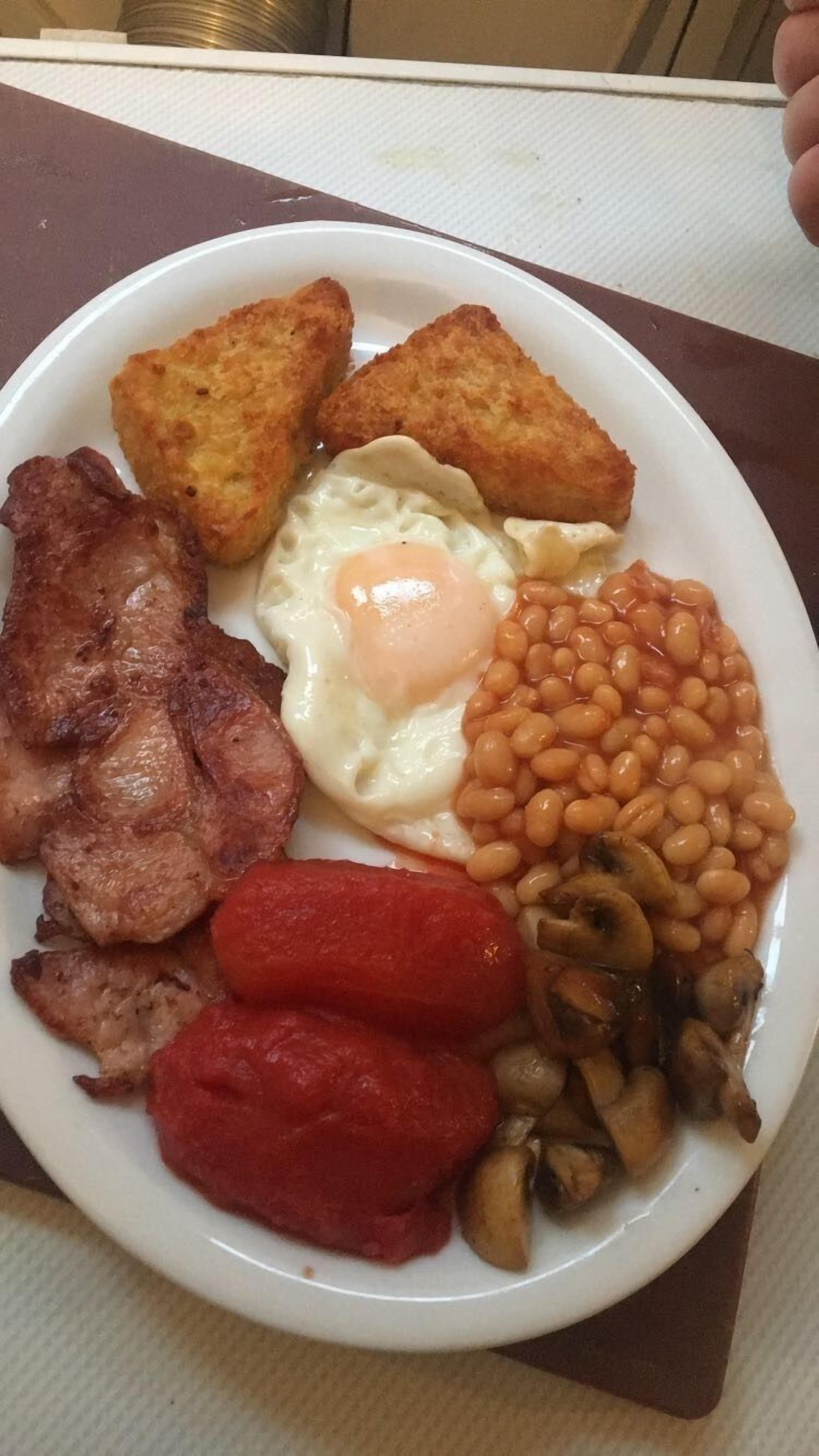 A plate of breakfast food including eggs, bacon, sausages, mushrooms, baked beans, and toast.