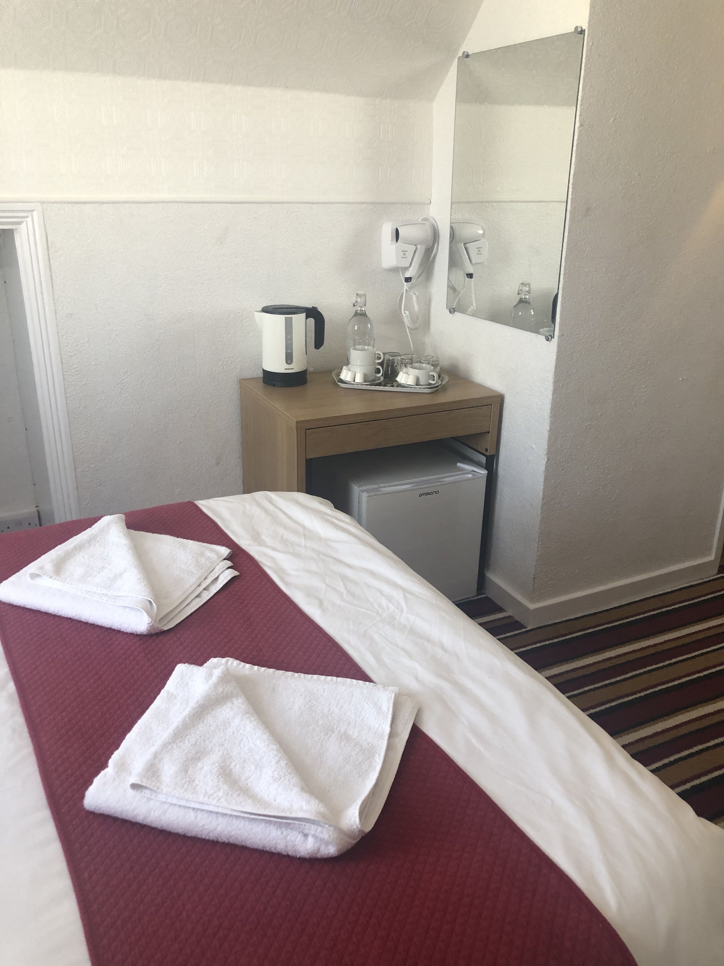 A hotel room with a bed, a small kitchenette, a mirror, and a coffee maker.