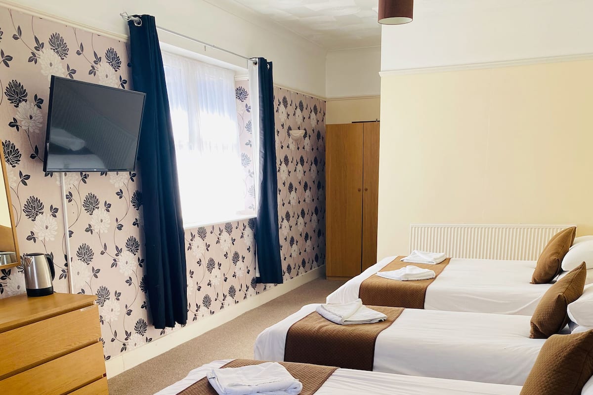 A hotel room with two beds, a wooden dresser, a flat-screen TV, and a window with curtains.