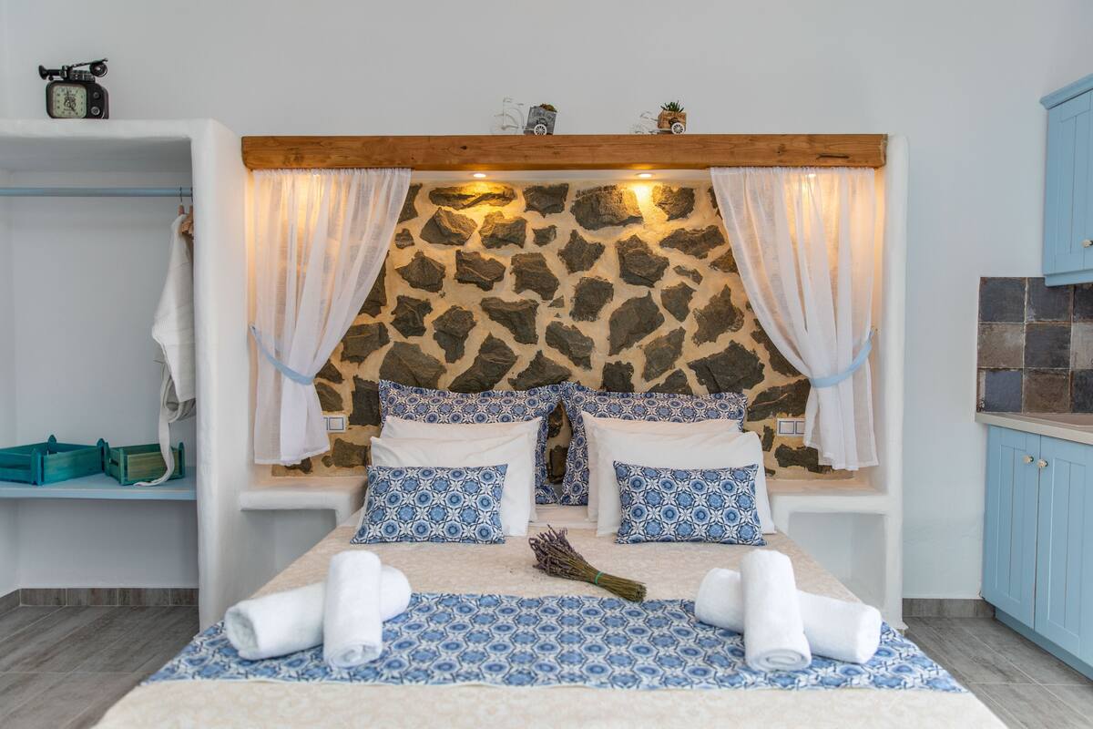 A bedroom with a stone-patterned headboard, a bed with blue and white patterned bedding, and a wooden ceiling.