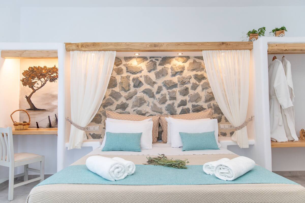 A bedroom with a stone wall, two beds with white and blue bedding, a wooden ceiling, and white curtains.