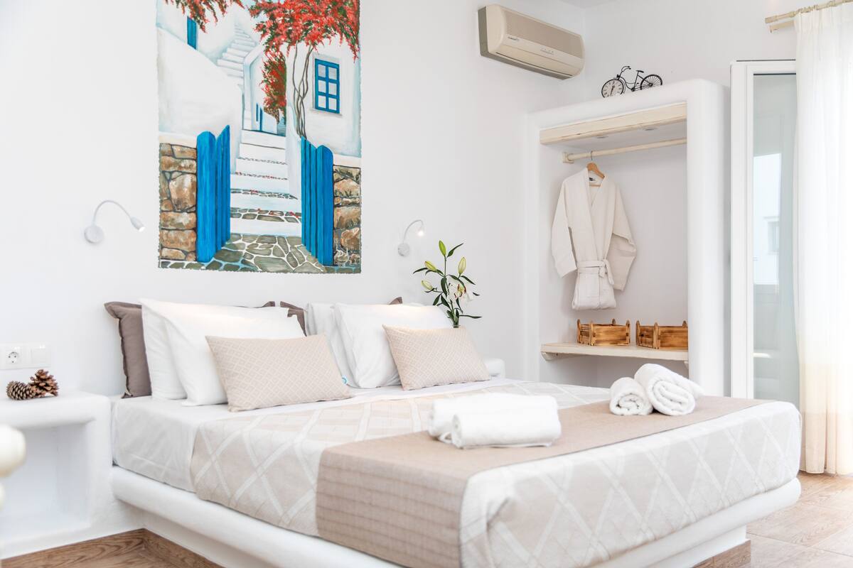 A bedroom with a bed, a painting, a robe, and a towel on the bed.