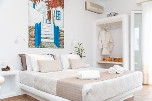 A bedroom with a bed, a painting, a robe, and a towel on the bed. - Arhontiko Studios (Naxos)