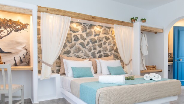 Une chambre à coucher avec une tête de lit en pierre, du linge de lit blanc et une vue sur la mer par la fenêtre.