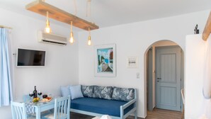 Une pièce comprenant un canapé, une table à manger avec des chaises, un téléviseur fixé au mur et une porte.