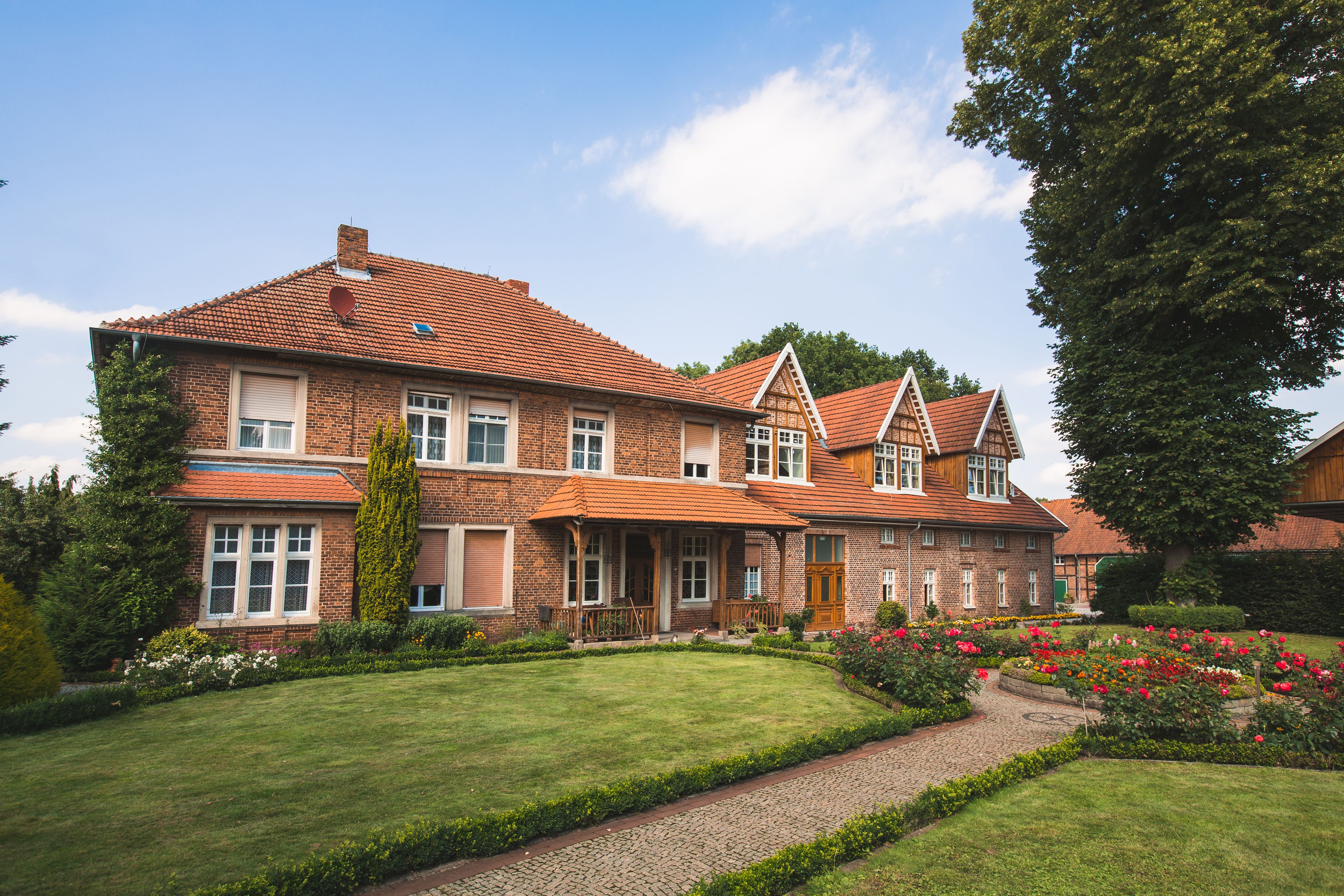 A large, two-story house with a brick exterior, multiple windows, and a well-maintained garden with flowers and a pathway.