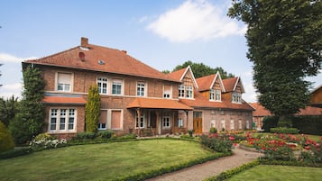 A large, two-story house with a brick exterior, multiple windows, and a well-maintained garden with flowers and a pathway.