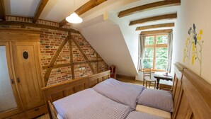 A bedroom with a sloped ceiling, exposed wooden beams, a brick wall, and a window with curtains. - Landhaus Schulze Osthoff (Warendorf)