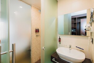 Un baño con mampara de vidrio, un lavabo blanco y un espejo encima.