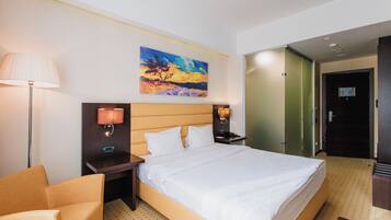 A hotel room with a large bed, a nightstand, a lamp, a painting on the wall, and a door to the right.
