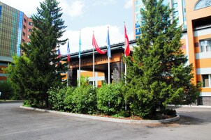 Un hotel con varias banderas, un árbol grande y un estacionamiento.