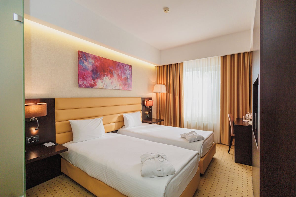 Een hotelkamer met twee bedden, een schilderij, een bureau met stoel en een televisie.