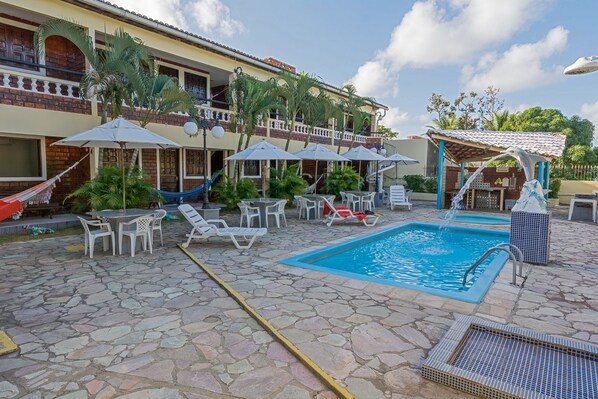 A pool area with lounge chairs, umbrellas, and a small water feature.