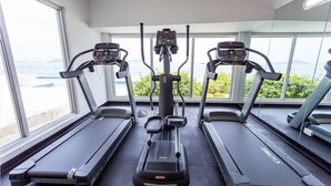 A gym with three treadmills, a central elliptical, and large windows offering a view of the outdoors. - Naos Luxury Rents (Panama City)