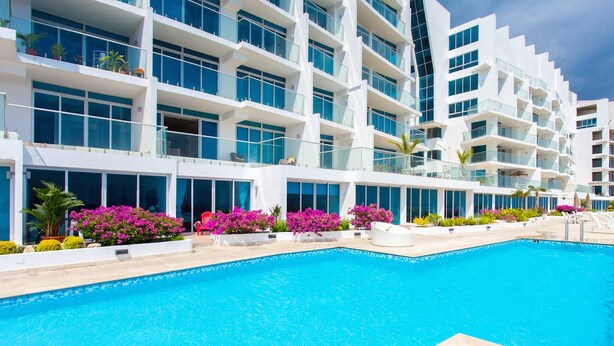 A modern hotel with a large swimming pool, multiple balconies, and lush landscaping. - Naos Luxury Rents (Panama City)