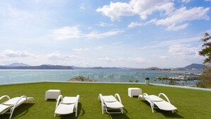 A poolside area with four white lounge chairs and a small white table, overlooking a body of water and distant mountains. - Naos Luxury Rents (Panama City)