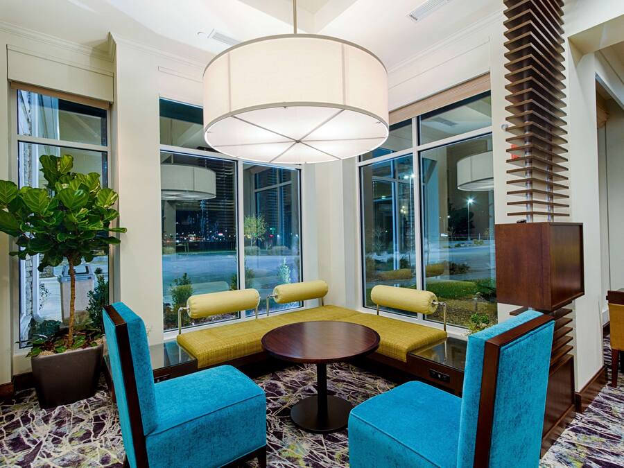 A modern lounge area with a round table, blue chairs, and a large window with a view of the city.