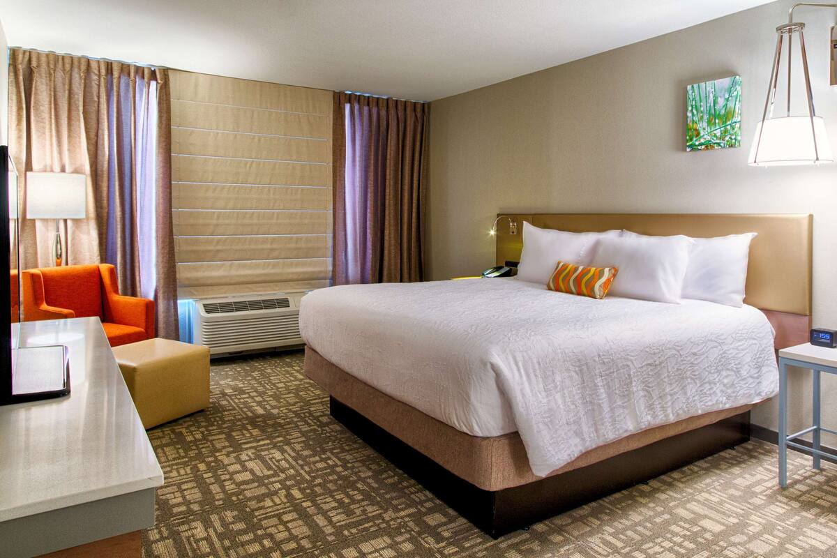 Une chambre d’hôtel avec un grand lit, un bureau avec une chaise, une lampe et un tableau au mur.