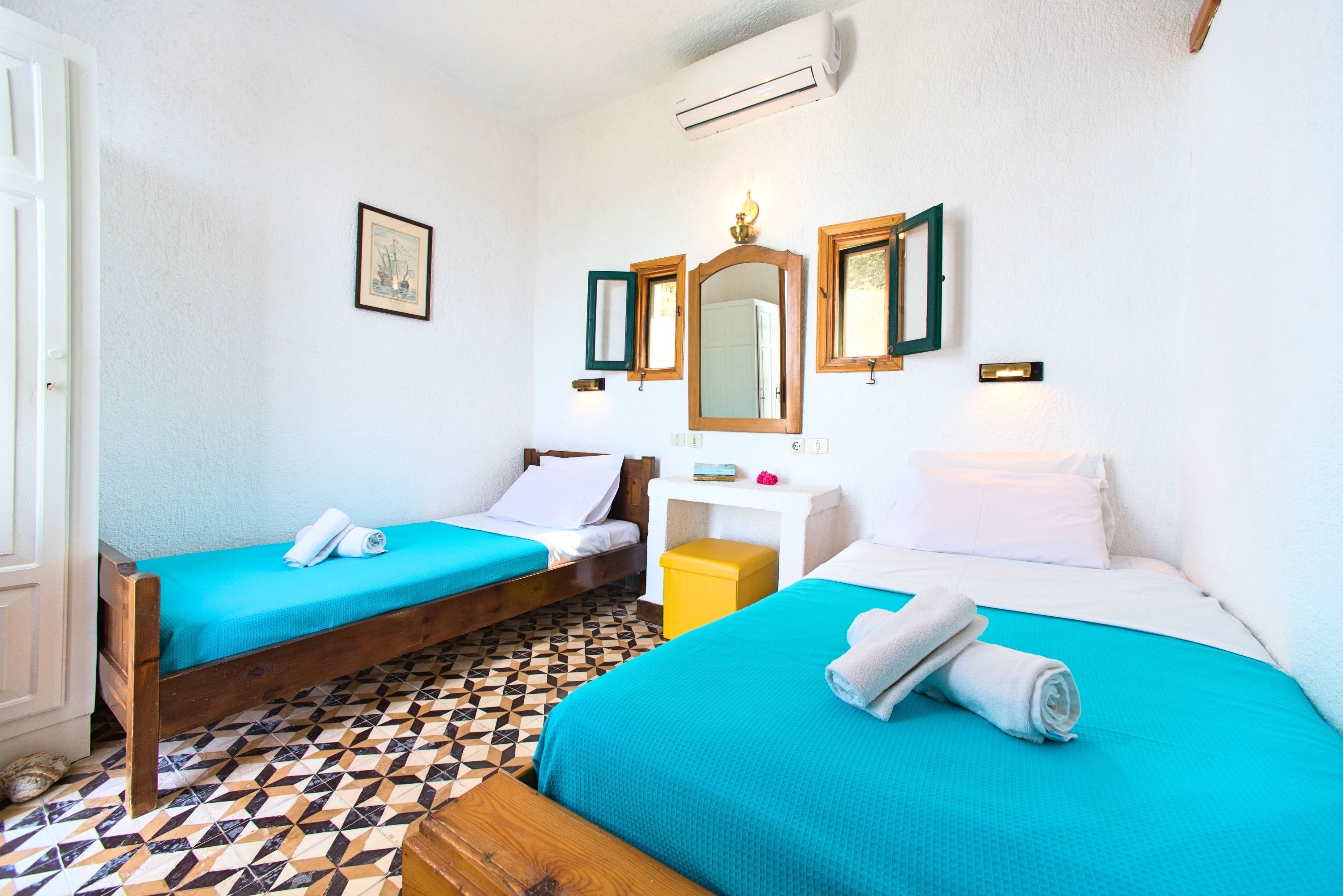 A room with two beds, a wooden floor, a white wall, and a mirror.