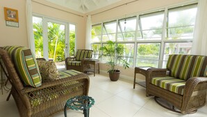 A sunroom with wicker furniture, large windows, and a potted plant. - Ocho Rios Getaway Villa at The Palms (Ocho Rios)