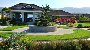 A house with a covered patio, a circular garden feature, and a well-maintained lawn. - Ocho Rios Getaway Villa at The Palms (Ocho Rios)