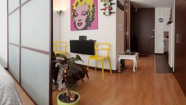 A modern living room with a flat-screen TV, two yellow chairs, a green plant, and a pink artwork on the wall. - Studio Chapinero 216 (Bogotá)