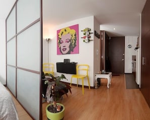 A modern living room with a flat-screen TV, two yellow chairs, a green plant, and a pink artwork on the wall.