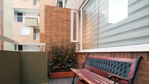 A bench in a courtyard with a brick wall and a window with blinds. - Studio Chapinero 216 (Bogotá)