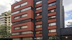 Um edifício moderno de vários andares com fachadas em tons de vermelho e cinza escuro, com grandes janelas e varandas.