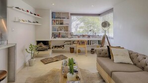 Uma sala de estar moderna com um sofá, uma mesa de centro com um cacto, uma estante de livros e uma área de jantar com mesa e cadeiras.