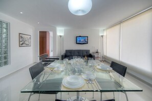 A modern dining area with a glass table set for six, a television mounted on the wall, and a view of the city through large windows. - Apartment Zona Rosa 2204 (Bogotá)