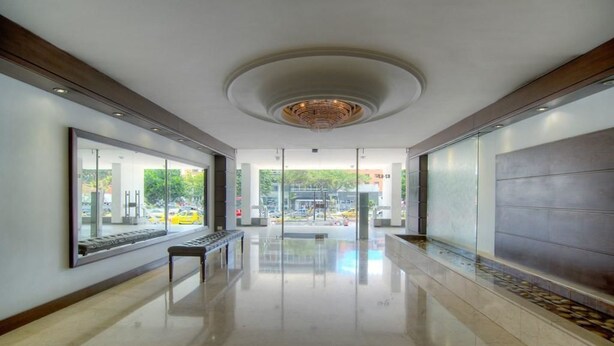 A modern hotel lobby with a reflective floor, a central bench, and large windows offering a view of the street. - Apartment Zona Rosa 2204 (Bogotá)