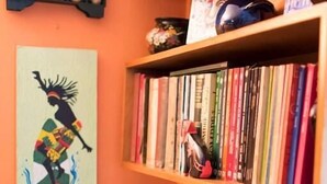 A room with a bookshelf filled with books, a decorative wall piece, and a shelf with teapots and a small figurine. - Apartment Chapinero 404 (Bogotá)