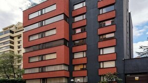 A multi-story building with a modern architectural design, featuring a combination of red and black facades, large windows, and a visible entrance with a small garden area. - Apartment Chapinero 404 (Bogotá)