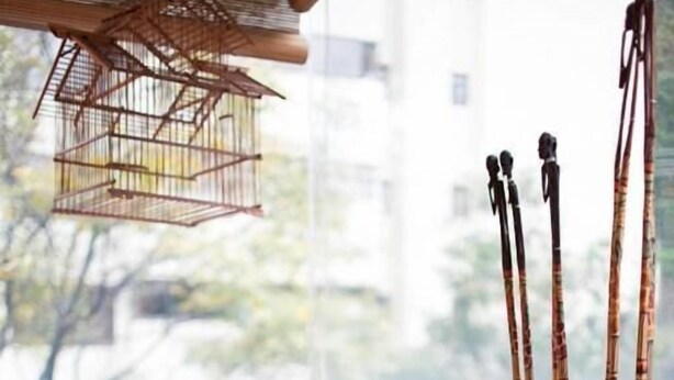 A room with a wooden bookshelf, a wicker chair, and a window with a view of buildings and trees. - Apartment Chapinero 404 (Bogotá)