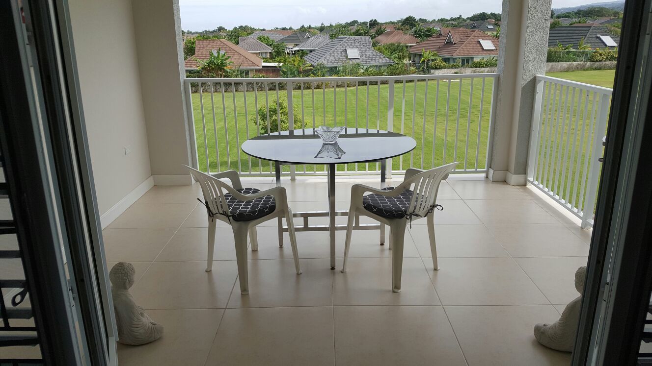 Ein Balkon mit Tisch und Stühlen, Blick auf eine grüne Rasenfläche und Häuser im Hintergrund.
