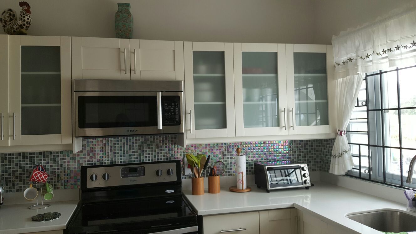 A kitchen with white cabinets, a Bosch microwave, a black stove, a toaster, and a window with curtains.