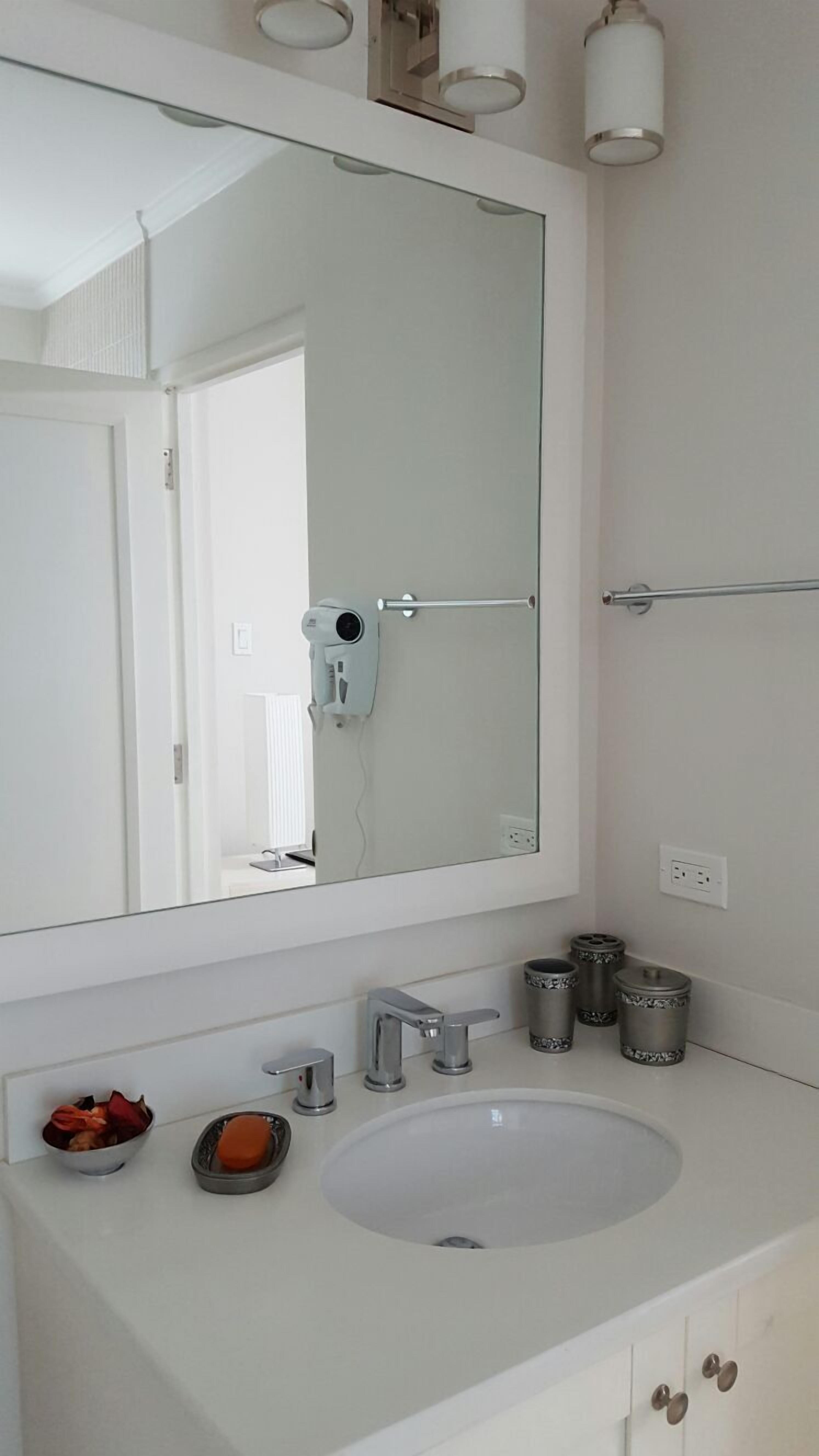A bathroom with a large mirror, a white sink, a hairdryer, and a towel rack.