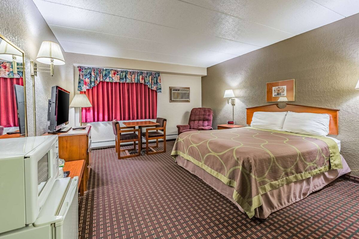 A hotel room with a bed, a desk with a chair, a television, a lamp, and a clock.